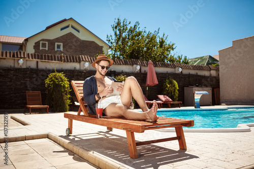 Young handsome man looking at tablet, sitting near swimming pool.