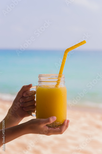 vitamin mango juice in a glass tube with an orange in his hand on the background of the turquoise sea in the tropics