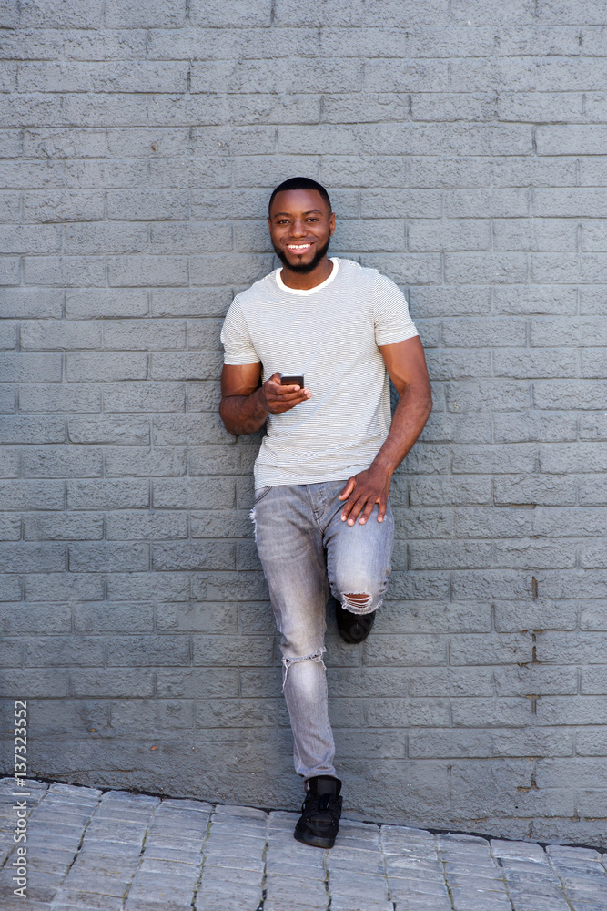 smiling man with smart phone leaning on gray wall smiling man with smart phone leaning on gray wall