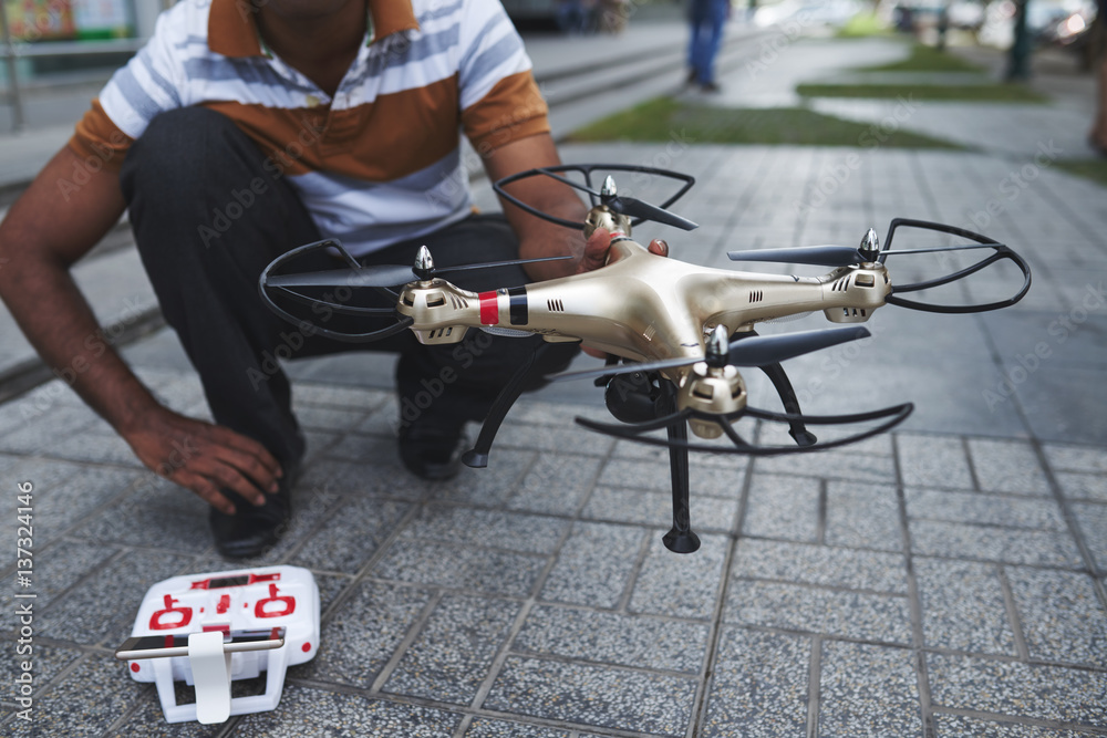 Close-up shot of man holding drone with four rotors in hand while sitting on haunches in city center