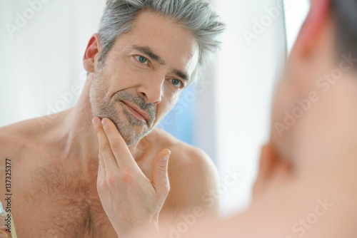 Portrait of mature man in front of mirror applying facial cream