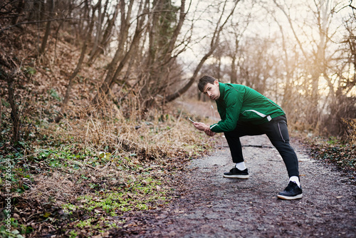 Athletic young man in sportswear stretching, after an endurance run on a forest road in sunset. © OctaCorp
