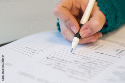 closeup of female hand signing document in blue sweater with black pen