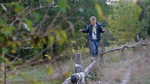 Little boy walk and balance on the log outdoor trying not to fall down.