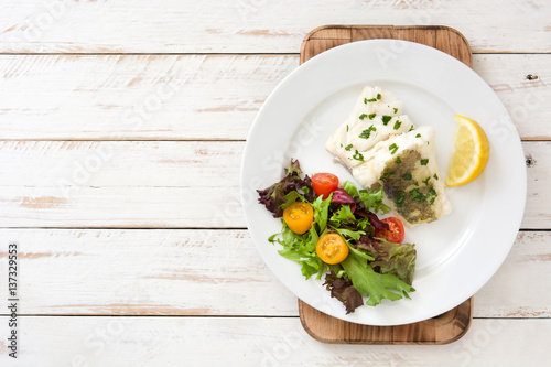 Fried cod fillet and salad in plate on white wooden background
 photo