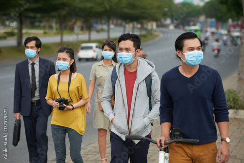 Asian people of different ages walking along street and protected themselves from flue with help of medical masks