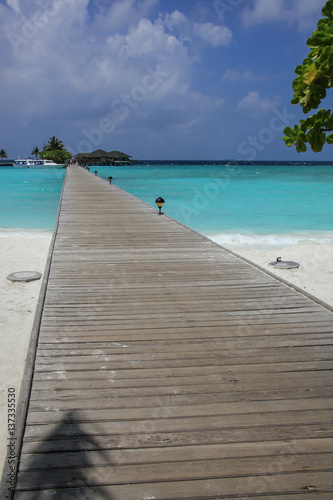 Wooden pier leads to bungalow complex on the island with anchored yacht, Maldives