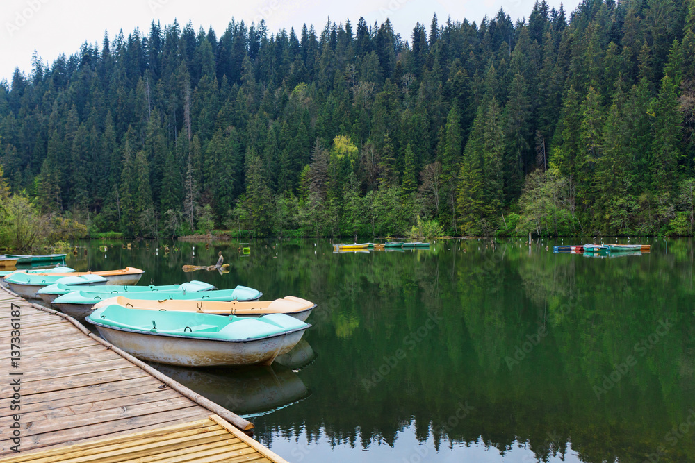 Boats at wooden relaxing area on the sovata lake in romania, rest area surrounded by historic forested mountains, rainy day, fog and reflection, near salt mine