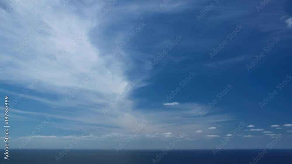 Timelapse of Clouds crossing the blue sky above the sea or ocean. The clouds are white and gray and cross from right to left. The clouds are reflected in the water. Timelapse of Clouds crossing the blue sky above the sea or ocean. The clouds are white and gray and cross from right to left. The clouds are reflected in the water.