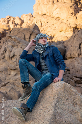 Man in a keffiyeh sitting on a rock in the desert