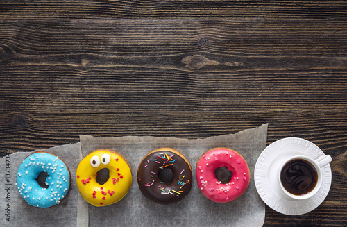 Multi-colored donuts with a cup of coffee on a wooden table. Copy space.