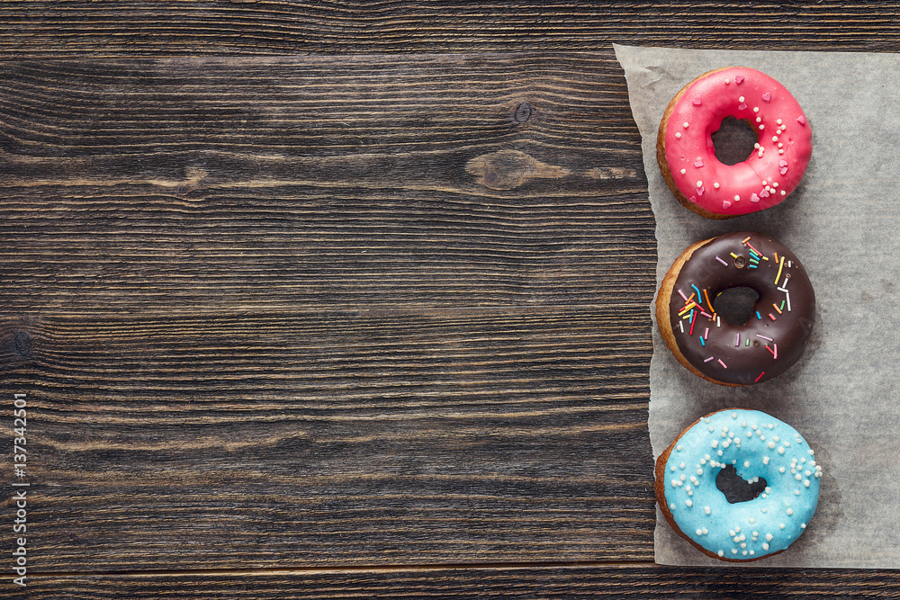 Multi-colored donuts with frosting on a dark wooden background. Space for text. Multi-colored donuts with frosting on a dark wooden background. Space for text.
