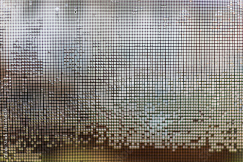 Metal mesh screen on window with rain water drops in squares