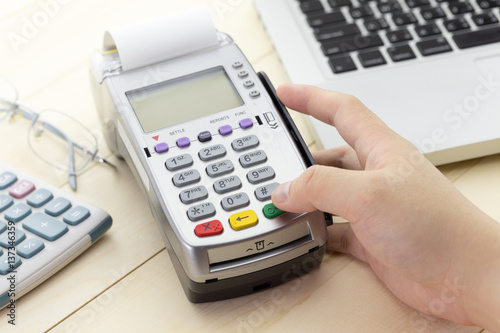 Cashier hand holding a Credit card over EDC machine or credit card terminal with calculator and glasses.