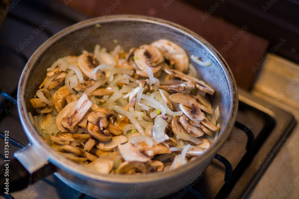 Mushrooms mushrooms stewed with onions and butter in a frying pan on a gas stove
