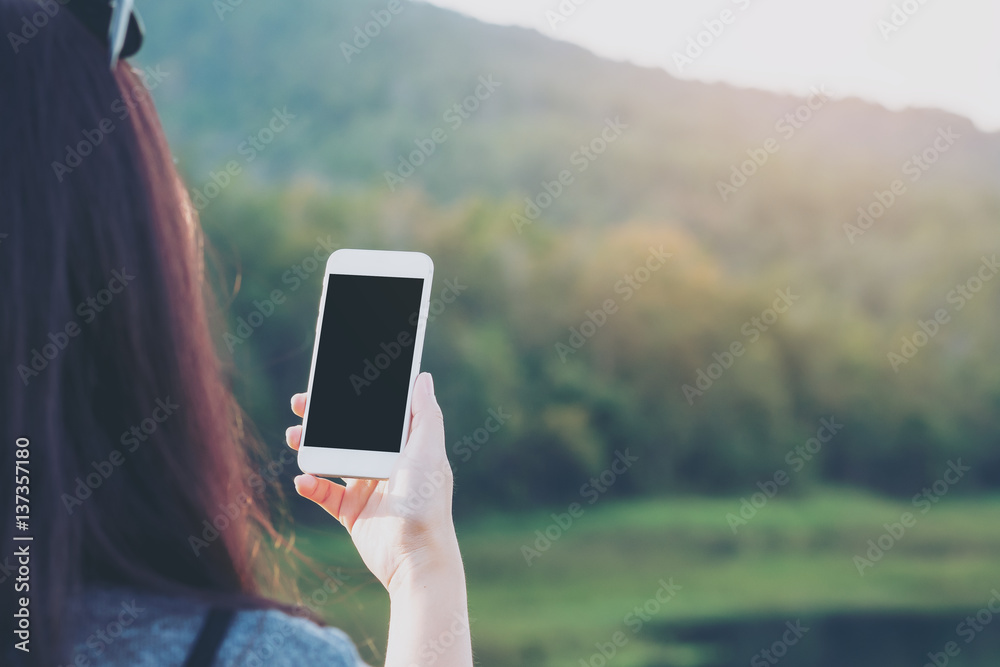 Mockup image of a woman using smart phone with blank black screen at outdoor with mountain and lake nature background Mockup image of a woman using smart phone with blank black screen at outdoor with mountain and lake nature background