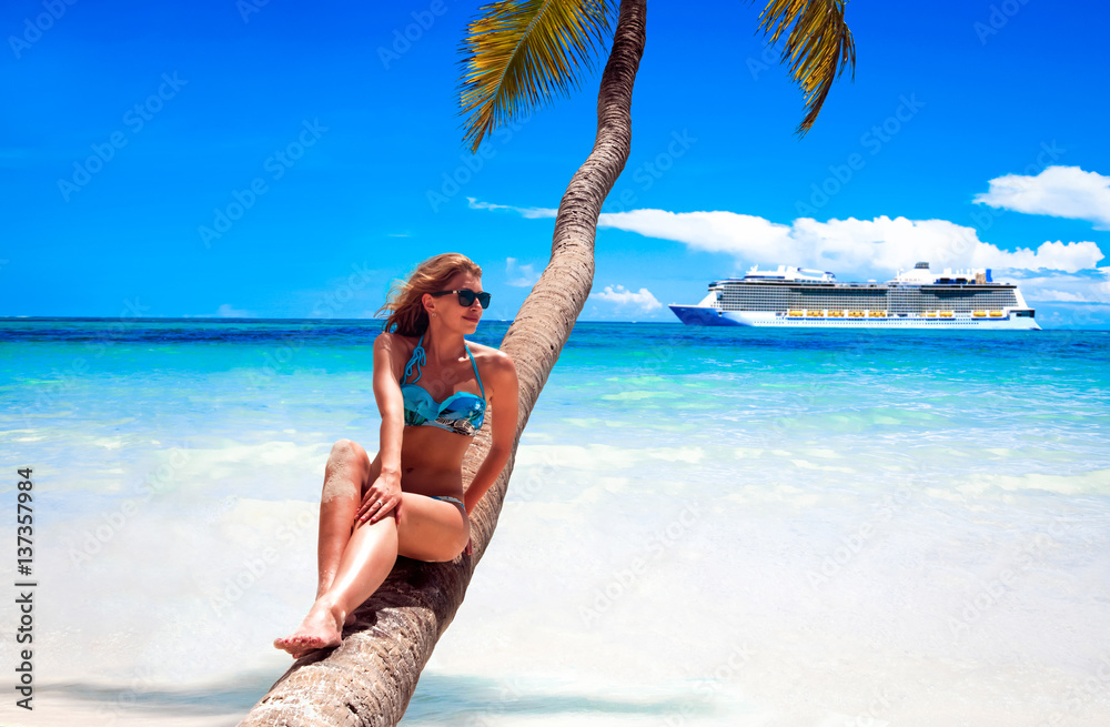Cruise vacation concept. Cruise ship in the sea near the tropical island with woman sitting on a coconut palm tree near the sea. Relaxing and enjoying vacation.