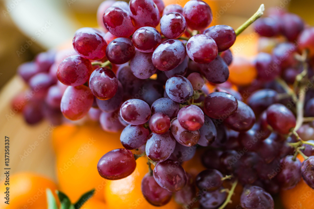 Closeup of a wooden bowl with ripe red grapes and raisins mandarins on kitchen table. Closeup of a wooden bowl with ripe red grapes and raisins mandarins on kitchen table.
