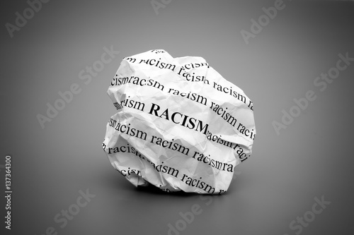 Crumpled paper ball with words Racism on gray background