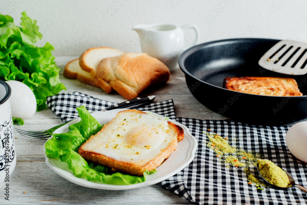 a delicious and hearty breakfast, fried eggs in a white toast with spices, peppers, lettuce, a cup of black coffee and milk on a wooden background 