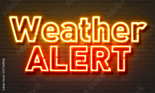 Weather alert neon sign on brick wall background.