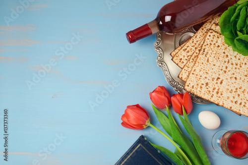 Passover holiday concept seder plate, matzoh and tulip flowers on wooden background. Top view from above