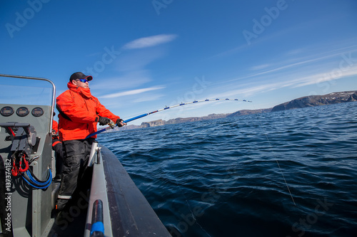 Man pulls out of Sea fish. Fishing rod bends. Red Jacket. sports glasses. fisherman
