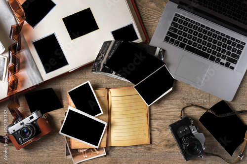 Old family photos on wooden background. Vintage pictures, camera, notepad and modern notebook. Flat lay. Blank photo frames