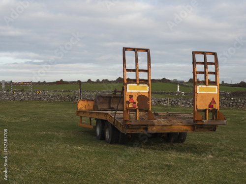 Old rusty orange trailer for heavy machinery in a field  