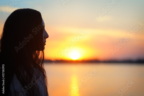 Profile of beautiful Asian woman looking at the sunset. Silhouette on a background of lake © Kseniia