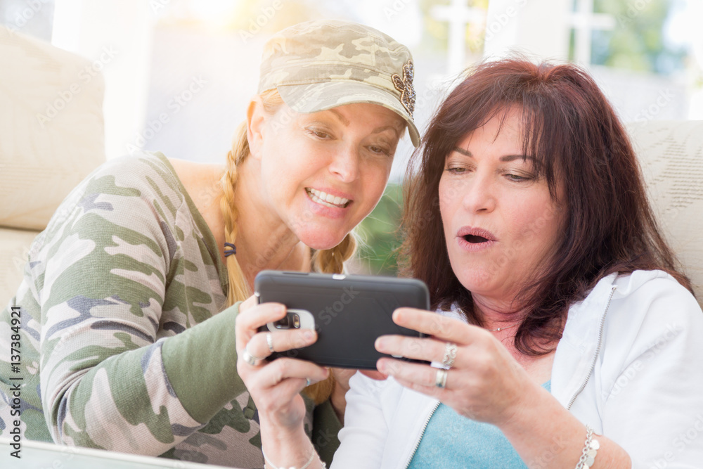 Two Female Friends Laugh While Using A Smart Phone on the Patio. Two Female Friends Laugh While Using A Smart Phone on the Patio.