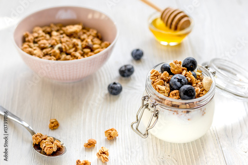 Homemade granola with blueberries in jar on white kitchen background