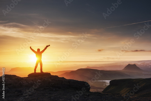 Happy man standing on a cliff at sunset