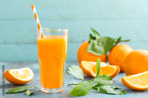 Obraz Sok pomarańczowy w szkle i świeżych owocach z liśćmi na drewnianym tle, witamina napoju lub koktajlu