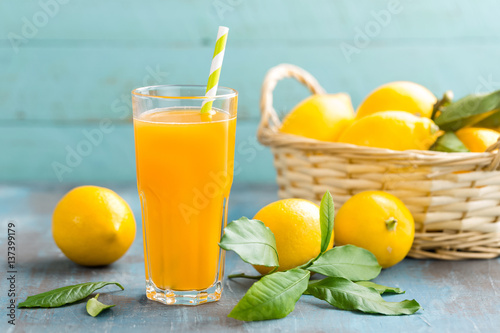 Lemon juice in glass and fresh fruits with leaves on wooden background, vitamin drink or cocktail