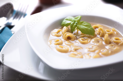 Dish of meat tortellini in soup with basil, with spoon and fork.
