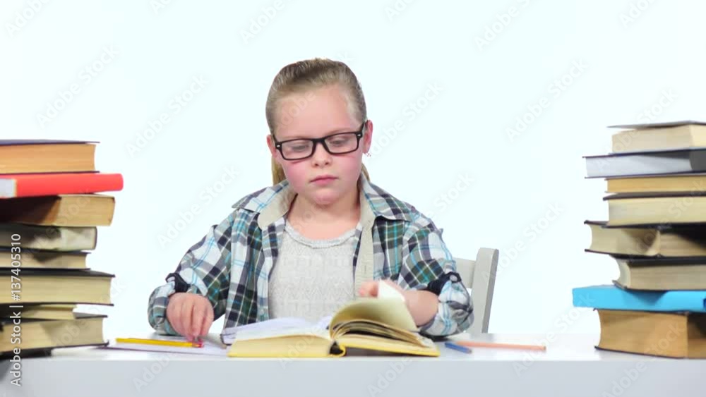 Girl sits at the table leafing through the book. White background Girl sits at the table leafing through the book. White background