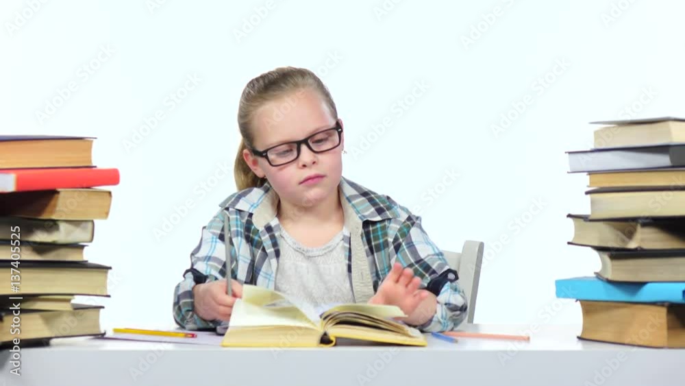 Girl sits at the table leafing through the book. White background Girl sits at the table leafing through the book. White background