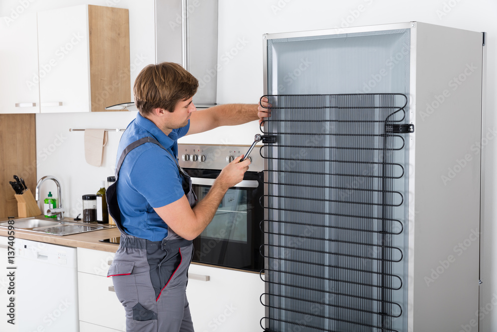 Serviceman Working On Fridge With Screwdriver Serviceman Working On Fridge With Screwdriver