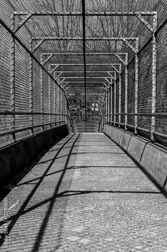Steel gate walkway. Walkway bridge. Industrial design. Steel gate frame. Chain link fence. Abstract design. Industrial art. Light and shadow. Urban photography. Street photography.