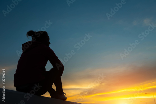 silhouette woman on road watching yellow and orange setting sun at sunset
