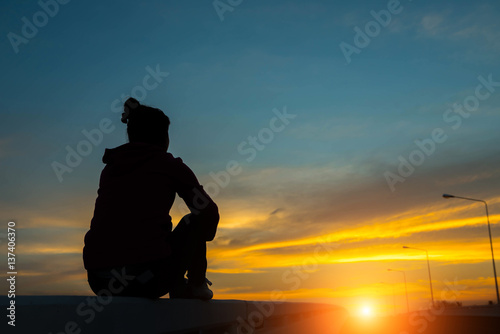 silhouette woman on road watching yellow and orange setting sun at sunset