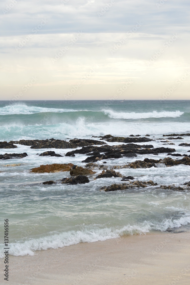 Sunset over the ocean, with waves breaking over the rocks