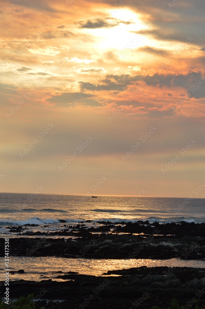 Fototapeta premium Sunset over the ocean, with waves breaking over the rocks