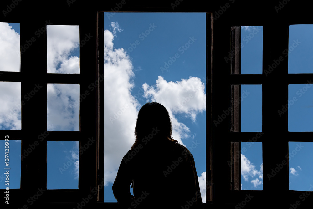 Silhouette young woman in the hotel, looking blue sky through the window