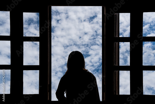 Silhouette young woman in the hotel, looking blue sky through the window