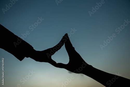 Concept or conceptual heart shape or symbol made of human or woman and man hand silhouette over a sky at sunset background for love