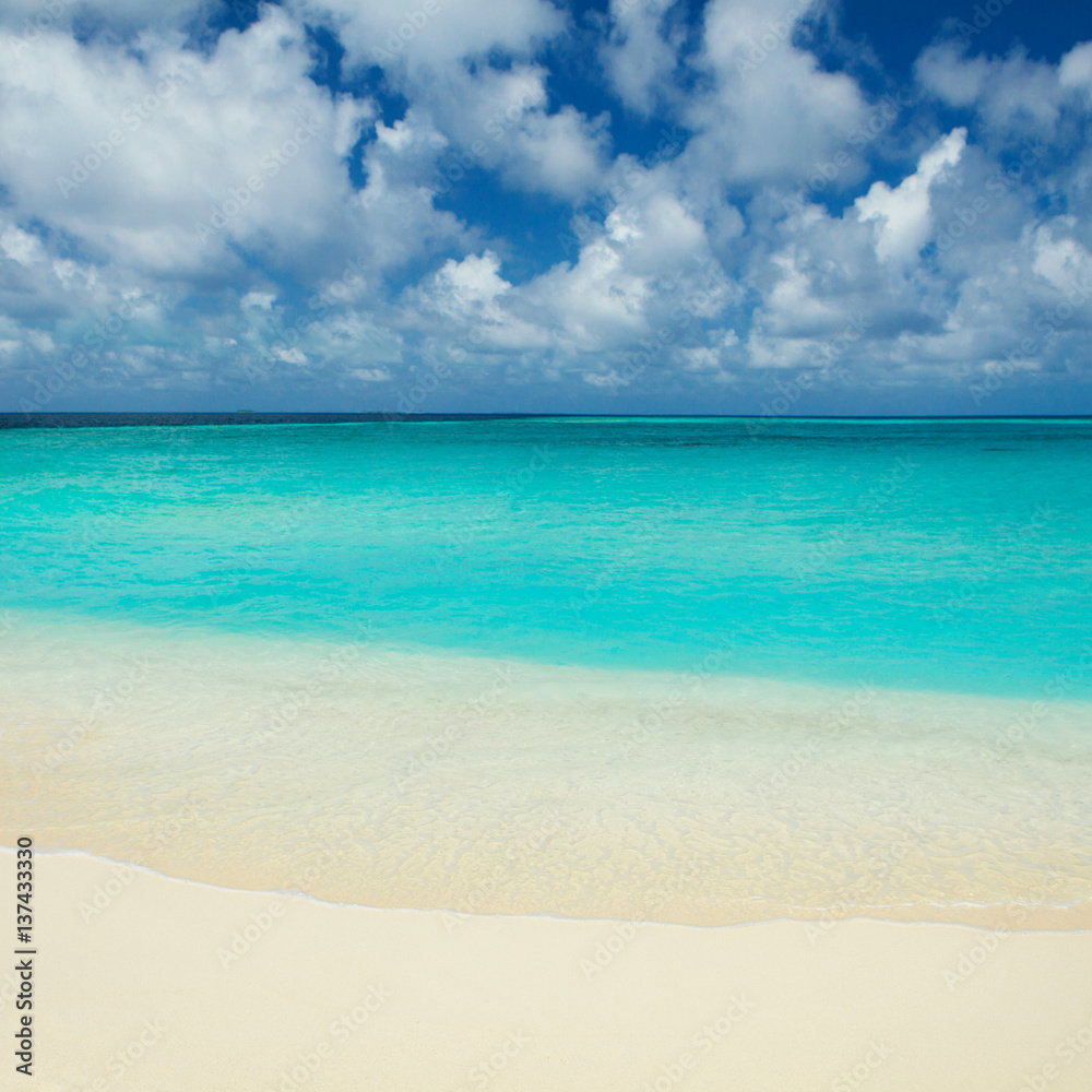 Tropical beach. Ocean waves and cloudy sky background. White sand and crystal-blue sea. Ocean water nature, beach relax. Summer sea vacation. Maldives islands sea background