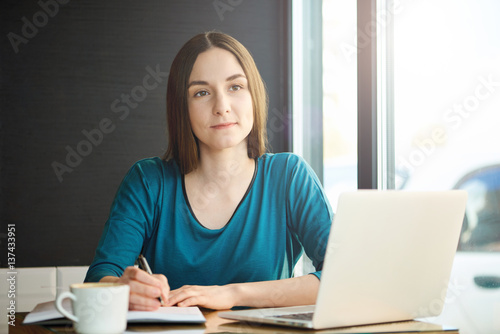 Young woman writing notes while working at cafe