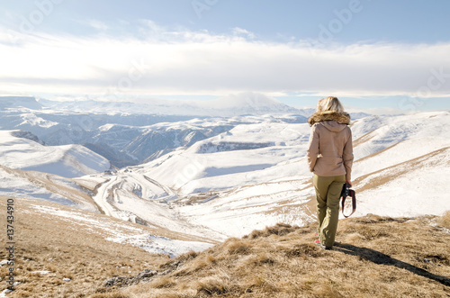 Beautiful blonde girl with a camera to take pictures of Caucasian mountains